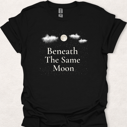 Nature-inspired moon and stars t-shirt featuring the phrase "Beneath The Same Moon" with a full moon, clouds, and a starry night sky.