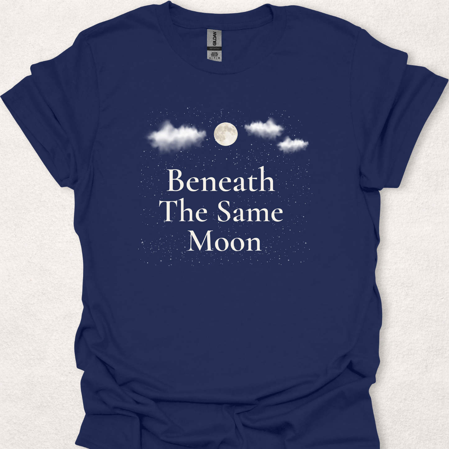 Beneath The Same Moon moon and stars t-shirt in navy featuring a full moon, clouds, and a starry night sky.