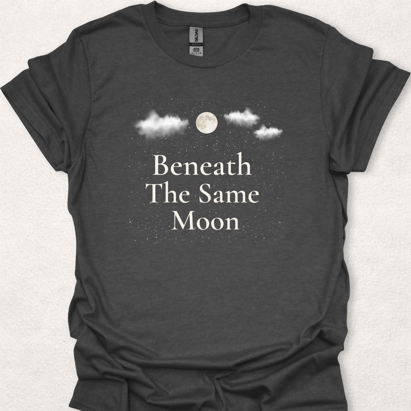 Beneath The Same Moon moon and stars t-shirt in dark heather featuring a full moon, clouds, and a starry night sky.