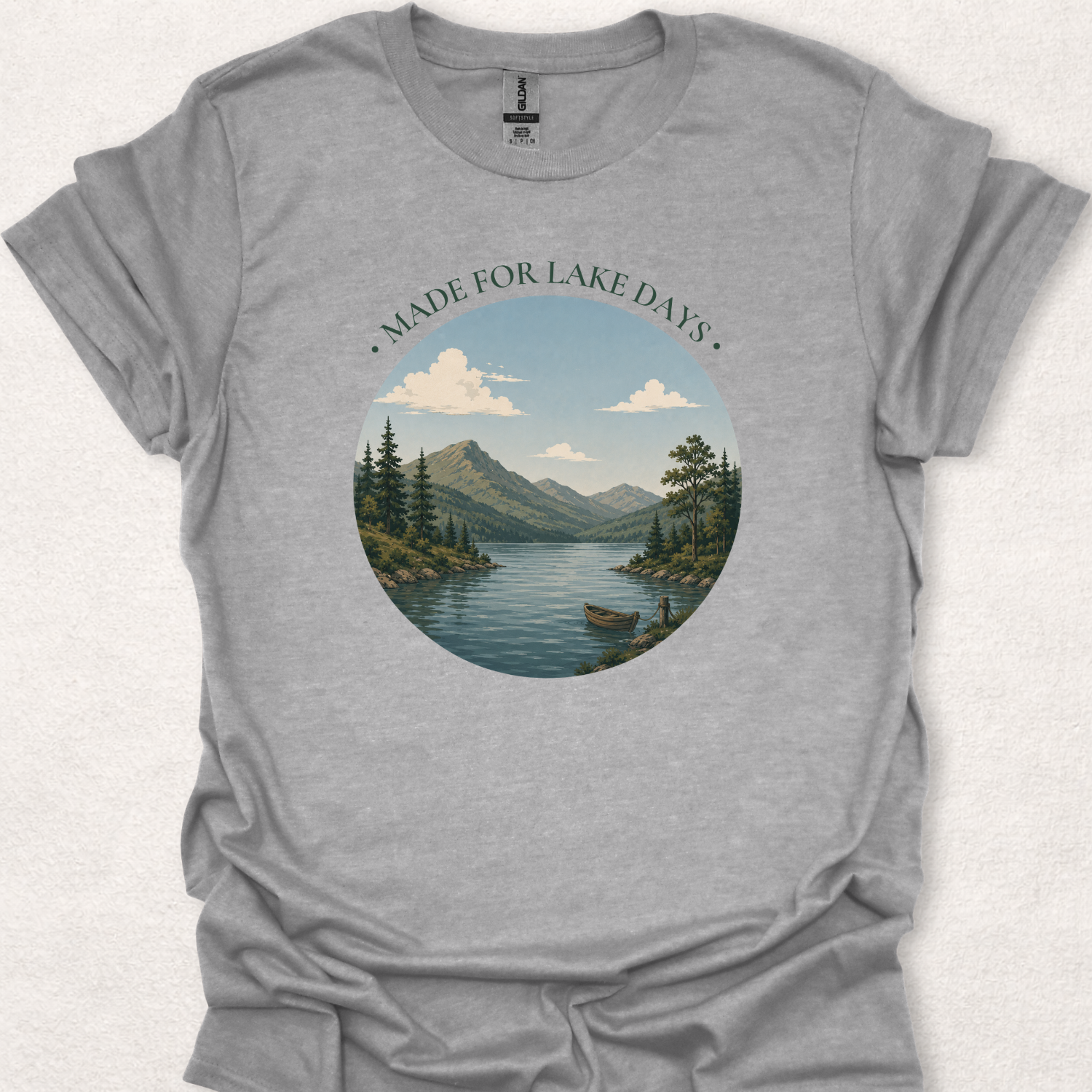 Sport gray t-shirt featuring the Made For Lake Days design with a peaceful mountain lake, small boat, evergreen trees, and vintage outdoor-inspired artwork.