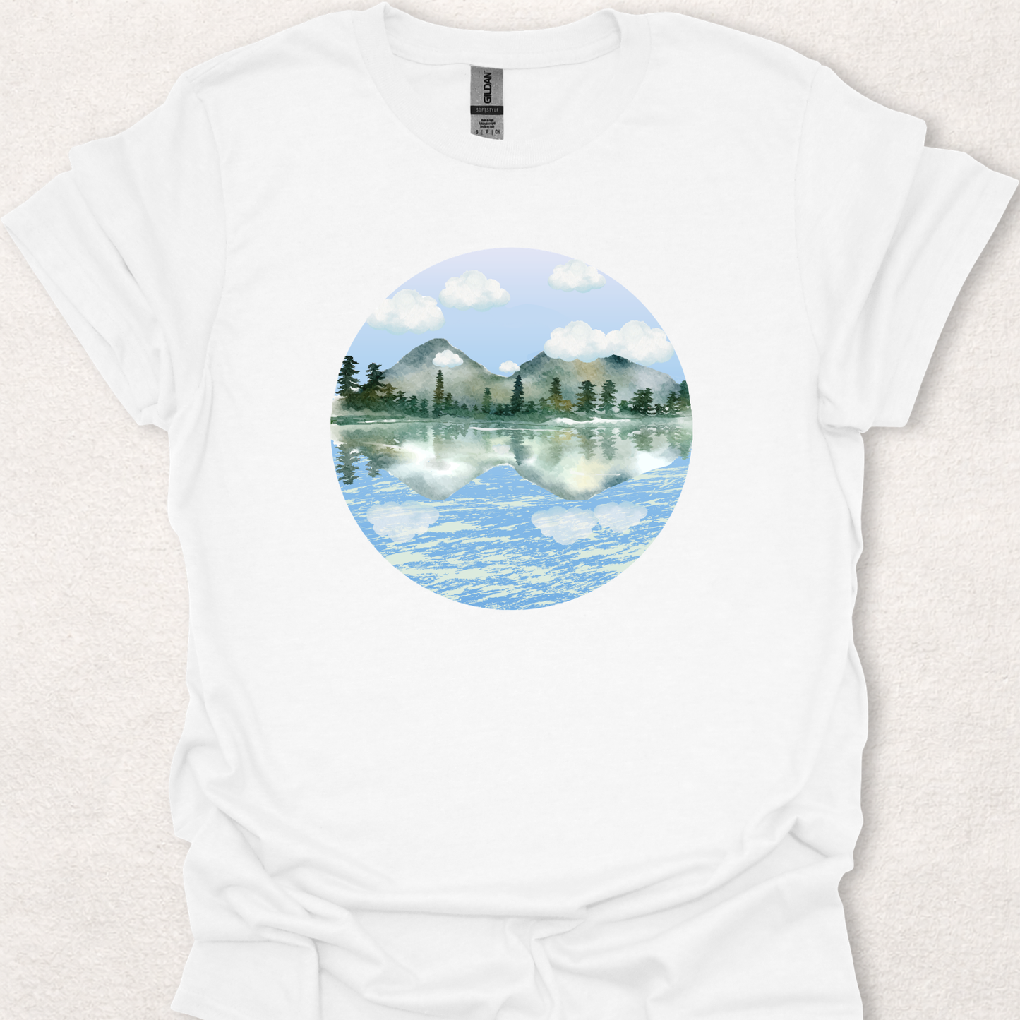 White t-shirt featuring the Stillwater watercolor mountain lake reflection design.