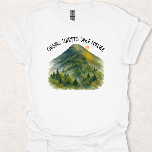 White t-shirt featuring the Chasing Summits Since Forever mountain graphic with a watercolor forest landscape and sunrise.