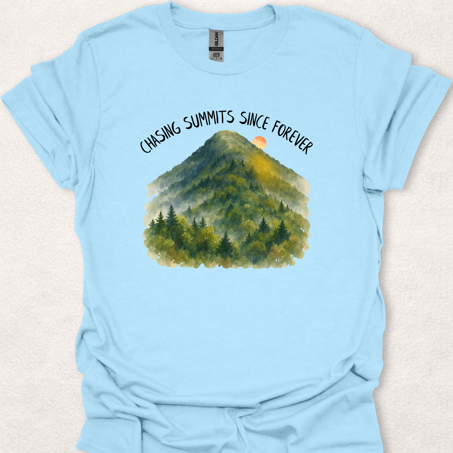 Light Blue t-shirt featuring the Chasing Summits Since Forever mountain graphic with a watercolor forest landscape and sunrise.
